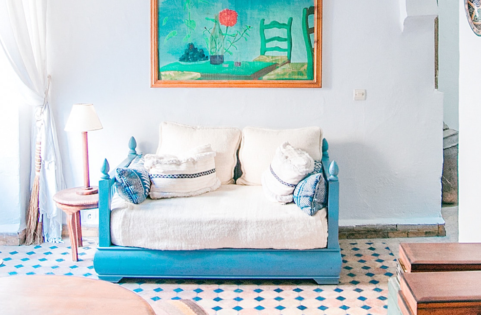 bedroom photo with blue and white bed at center below a large green kitchen table painting