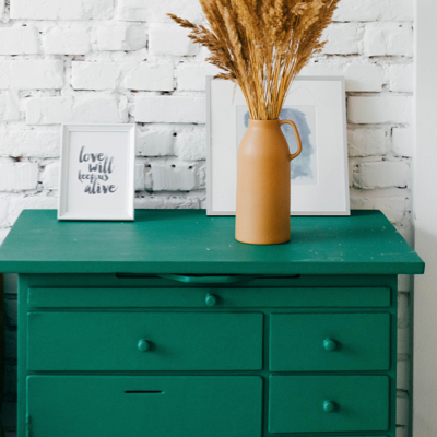 photo of green end table with brown jug holding brown plants on top